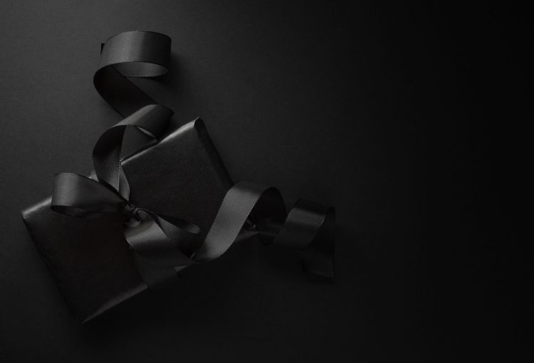 Black gift on dark background Gift wrapped in black paper with black bow on dark background. View from above.